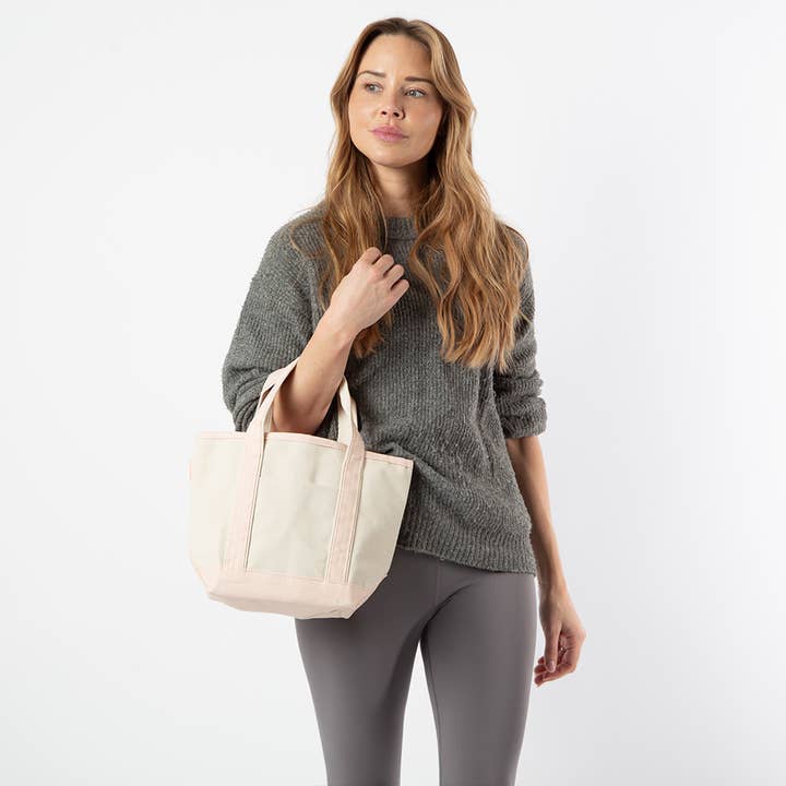 a person wearing grey pants and sweater holding off white tote with pale pink handles and trim