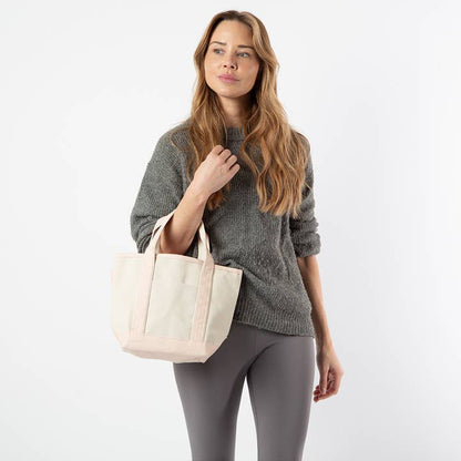 a person wearing grey pants and sweater holding off white tote with pale pink handles and trim
