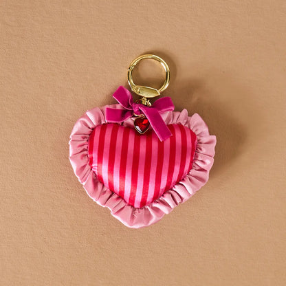 pink and red Heart-shaped bag charm with a gold ring on a beige background