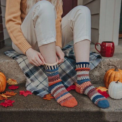 person sitting on porch steps  with pumpkins on it and putting on Nutmeg Crew Socks