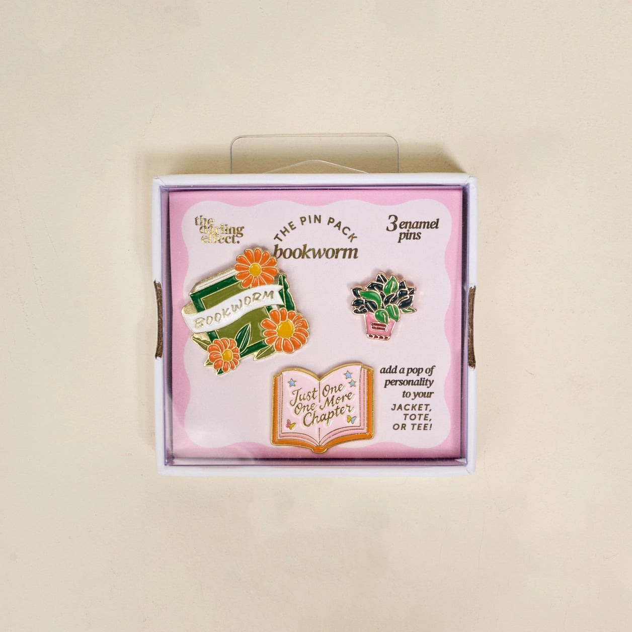 Box of 'Bookworm' themed enamel pins with decorative elements on a beige background