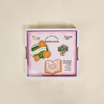 Box of 'Bookworm' themed enamel pins with decorative elements on a beige background