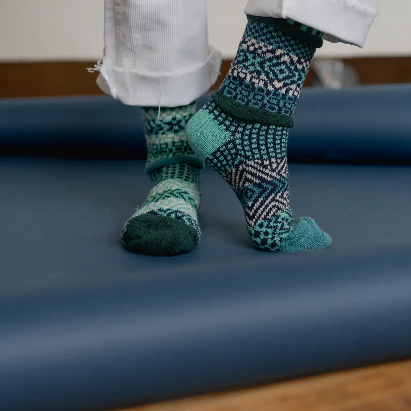 person wearing white pants rolled up at the hem and Evergreen Crew Socks standing on a blue mat
