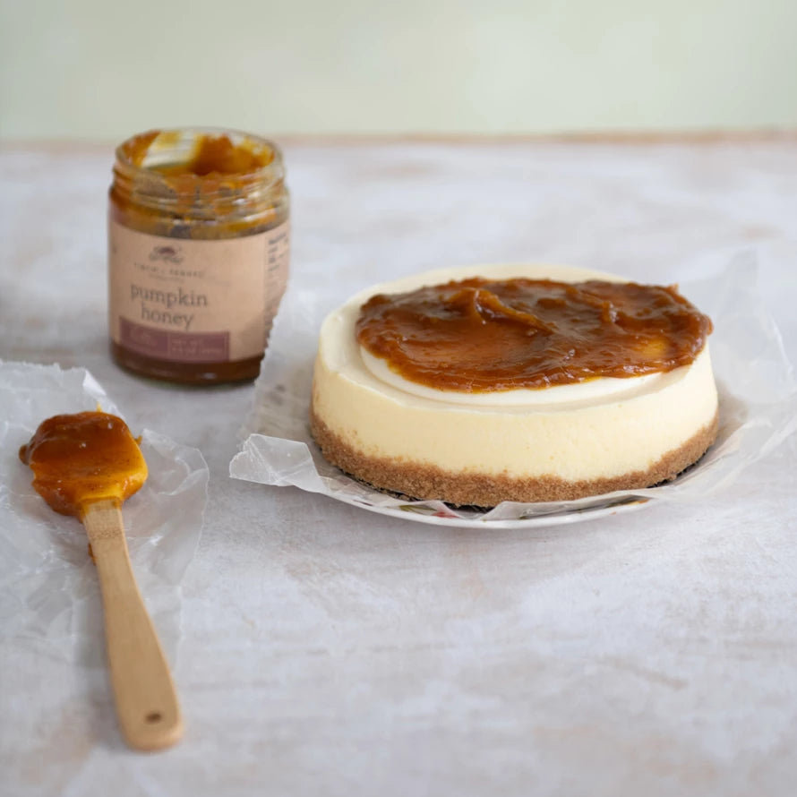 Cheesecake with pumpkin honey on a white surface, accompanied by a jar of pumpkin honey and a spoon.