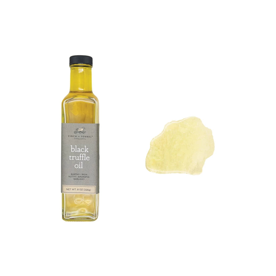 bottle of Black Truffle Oil with a puddle of it on a white background.