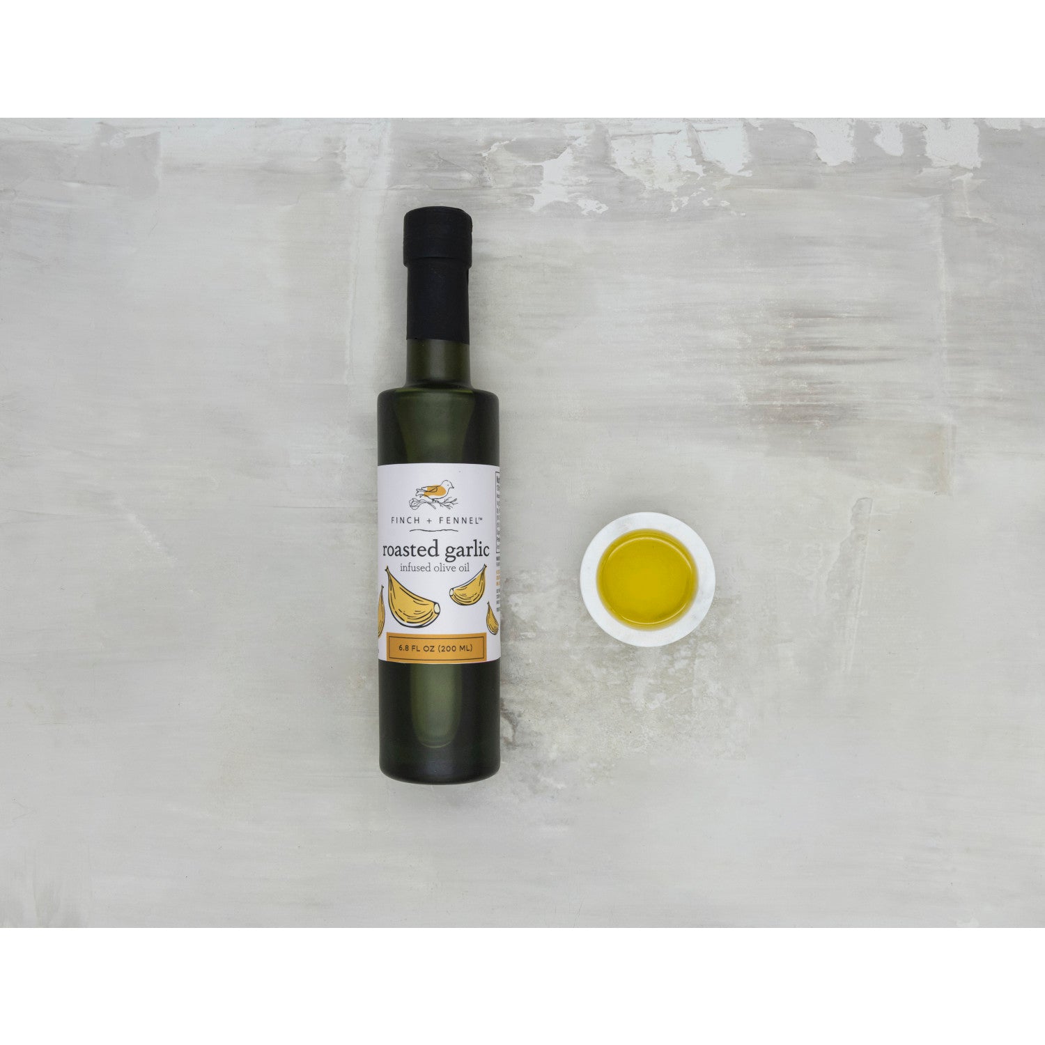 Bottle of roasted garlic oil with a small dish of oil on a light gray background