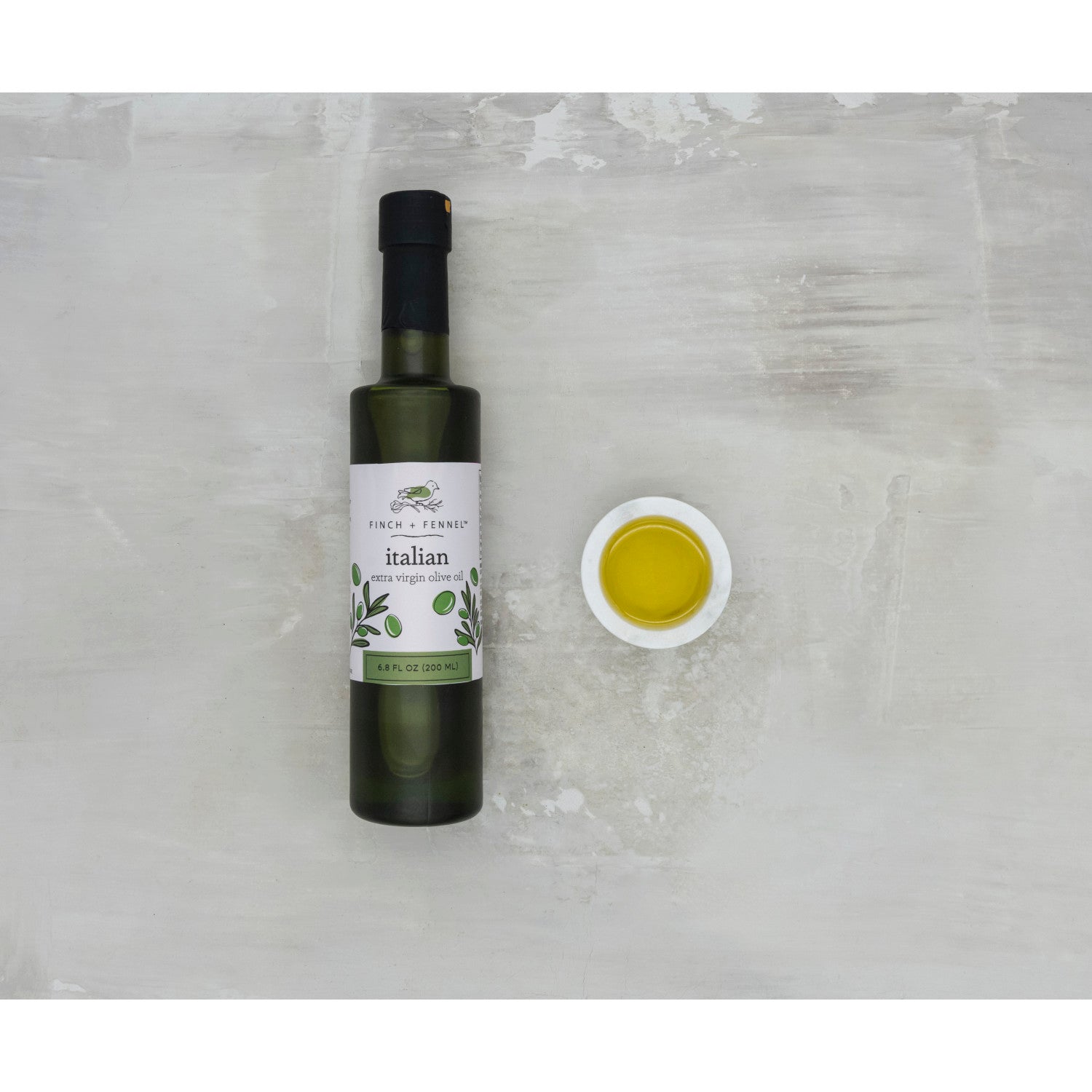 Bottle of Italian olive oil with a small dish of oil on a textured surface