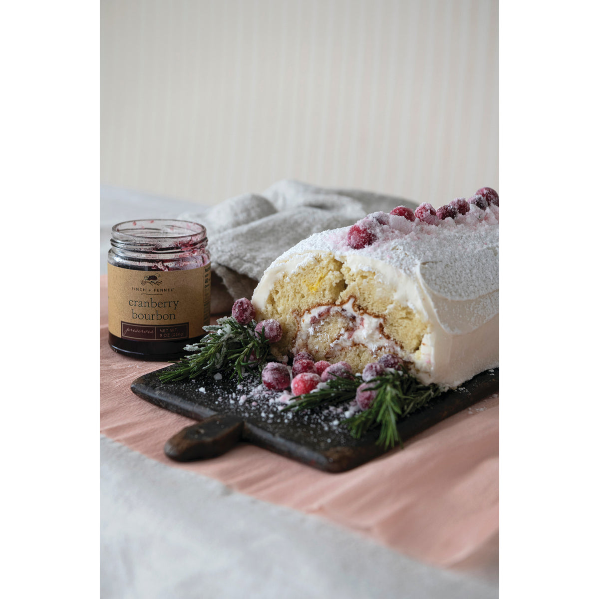 cake roll with white icing and cranberry garnish set next to a jar of cranberry bourbon preserves