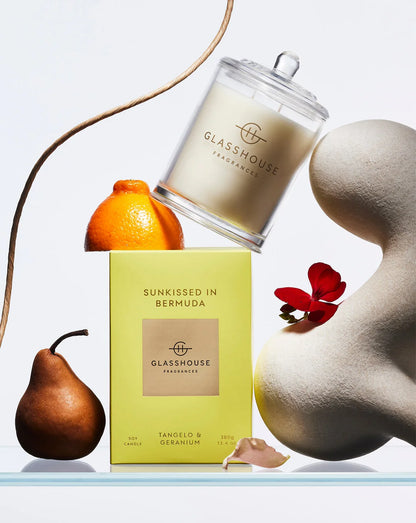 Glasshouse Fragrances candle and packaging artfully arranged with a pear, orange, and flower on a light background