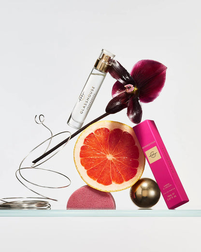perfume bottle, pink box, orchid flower, and grapefruit arranged artfully on a light background