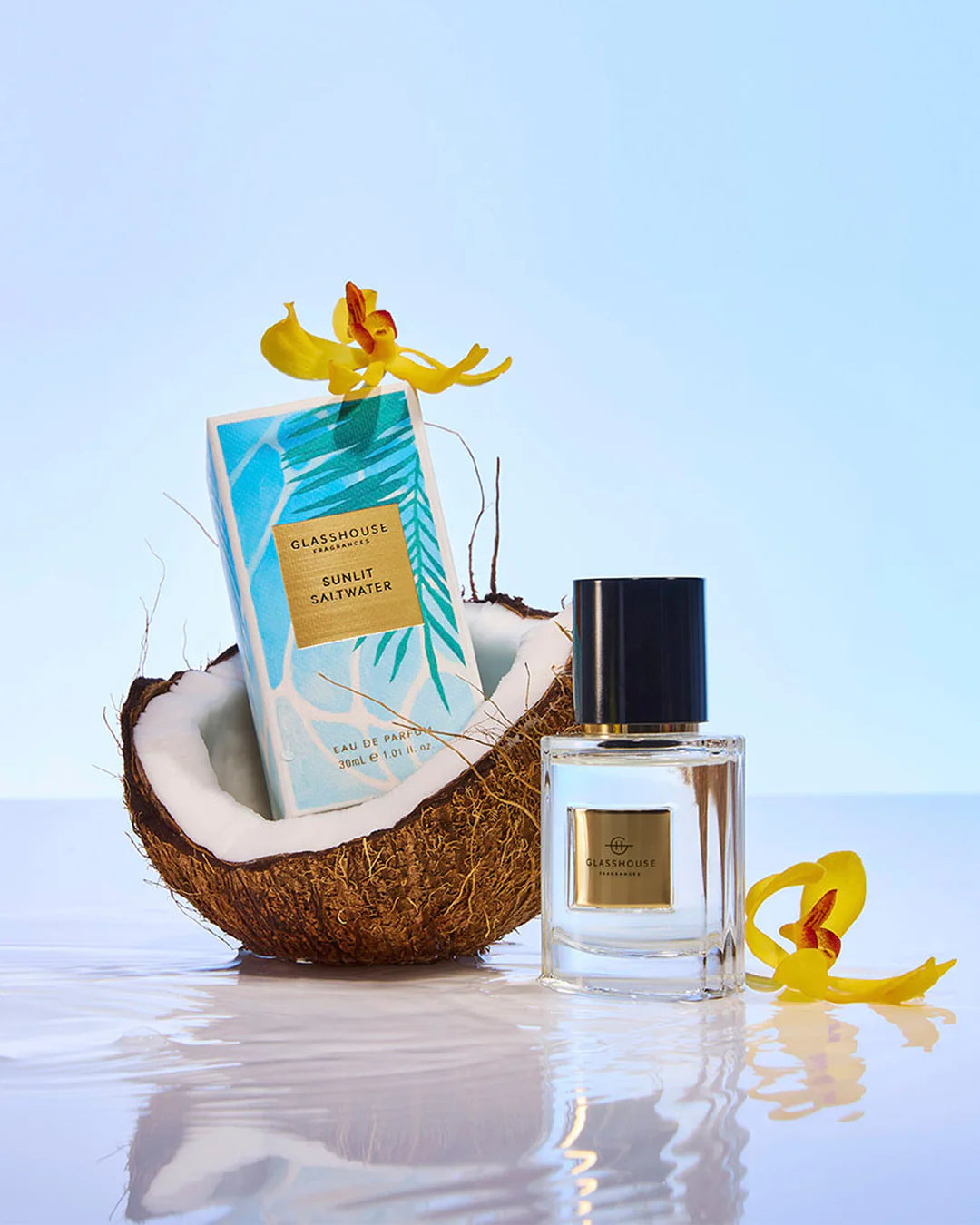 Perfume bottle and packaging with a coconut and flowers on a watery surface