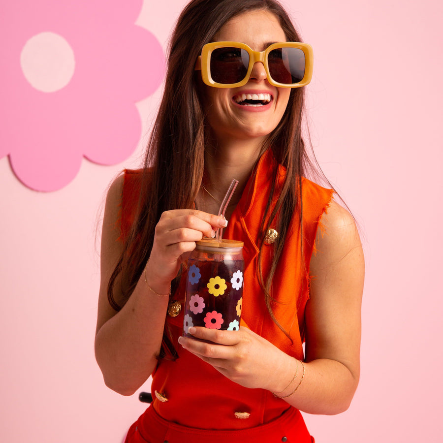 person wearing orange outfit and big sunglasses smiling and holding daisy glass.