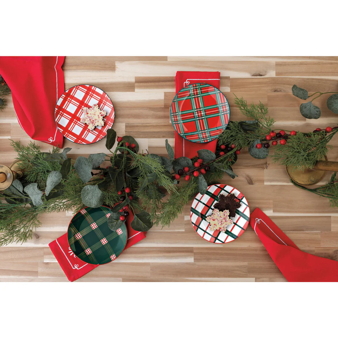 4 styles of holiday plaid plates arranged on  a table with greenery and napkins, 2 plates have cookie on them.