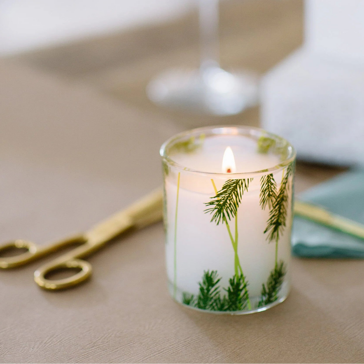 Candle with greenery design on a table with a blurred background