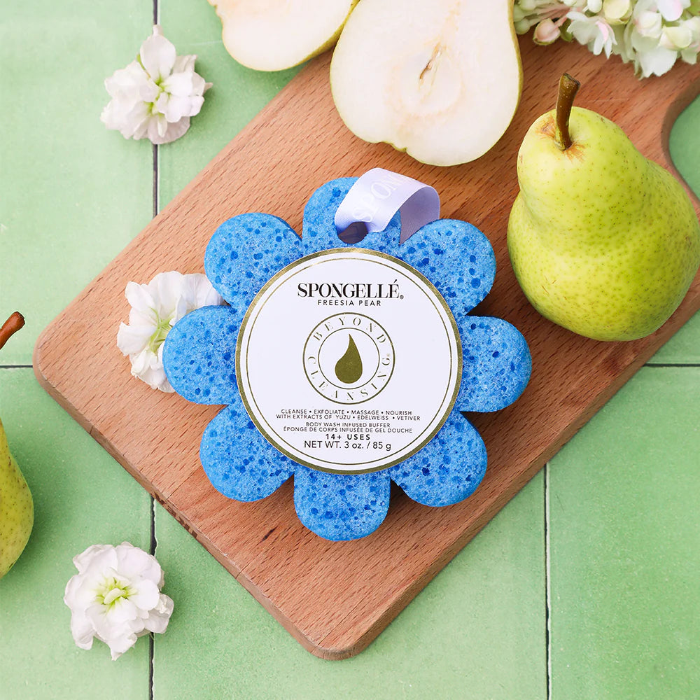 Blue flower-shaped sponge with Spongellé branding on a wooden cutting board with pears and flowers.