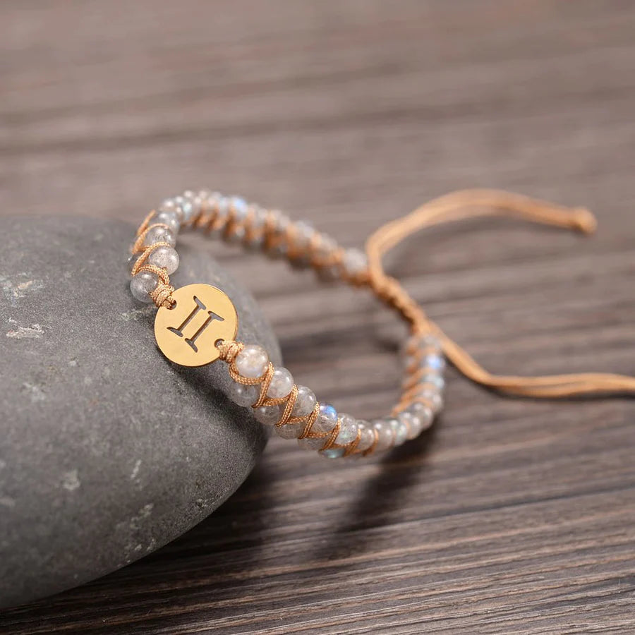 gemini bracelet draped on a stone on a wooden table.