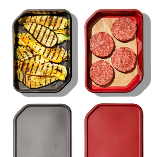 top view of the red and gray carry systems displayed with the lids off revealing grilled squash and the other with prepped hamburgers and displayed against a white background