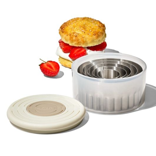 cutter set in its case with lid next to it and a biscuit filled with cream and strawberries behind it.