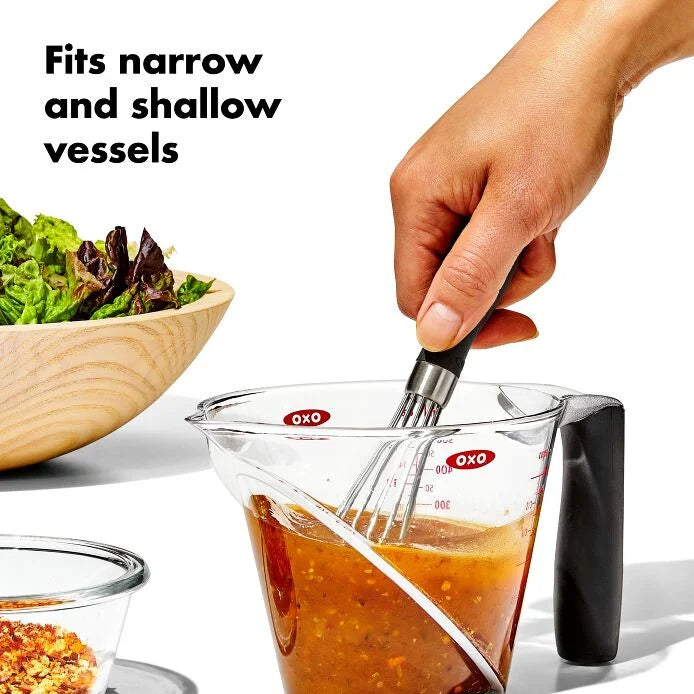 hand holding Mini Whisk in a measuring cup and mixing ingredients