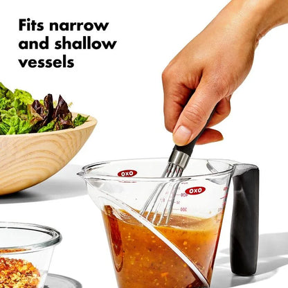 hand holding Mini Whisk in a measuring cup and mixing ingredients