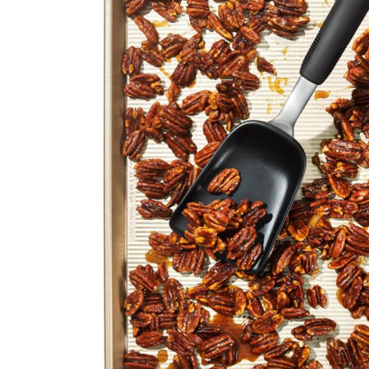 top view of sheet pan scoop scooping toasted pecans fron sheet pan.