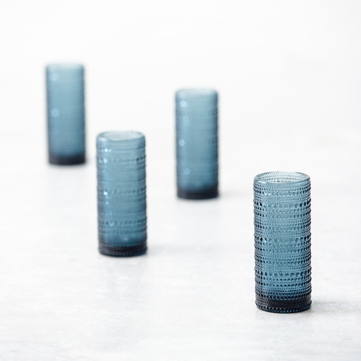 4 cornflower jupiter collins glasses arranged on a countertop.