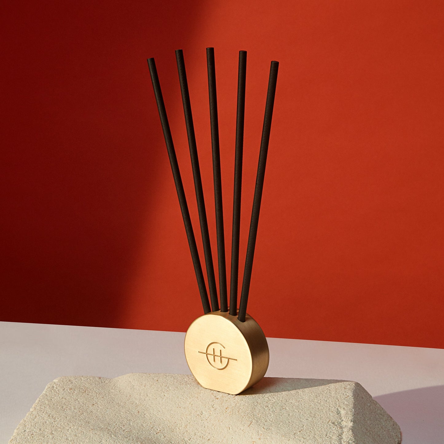 five Scent Stems displayed in the gold metal vessel on a table against a red wall