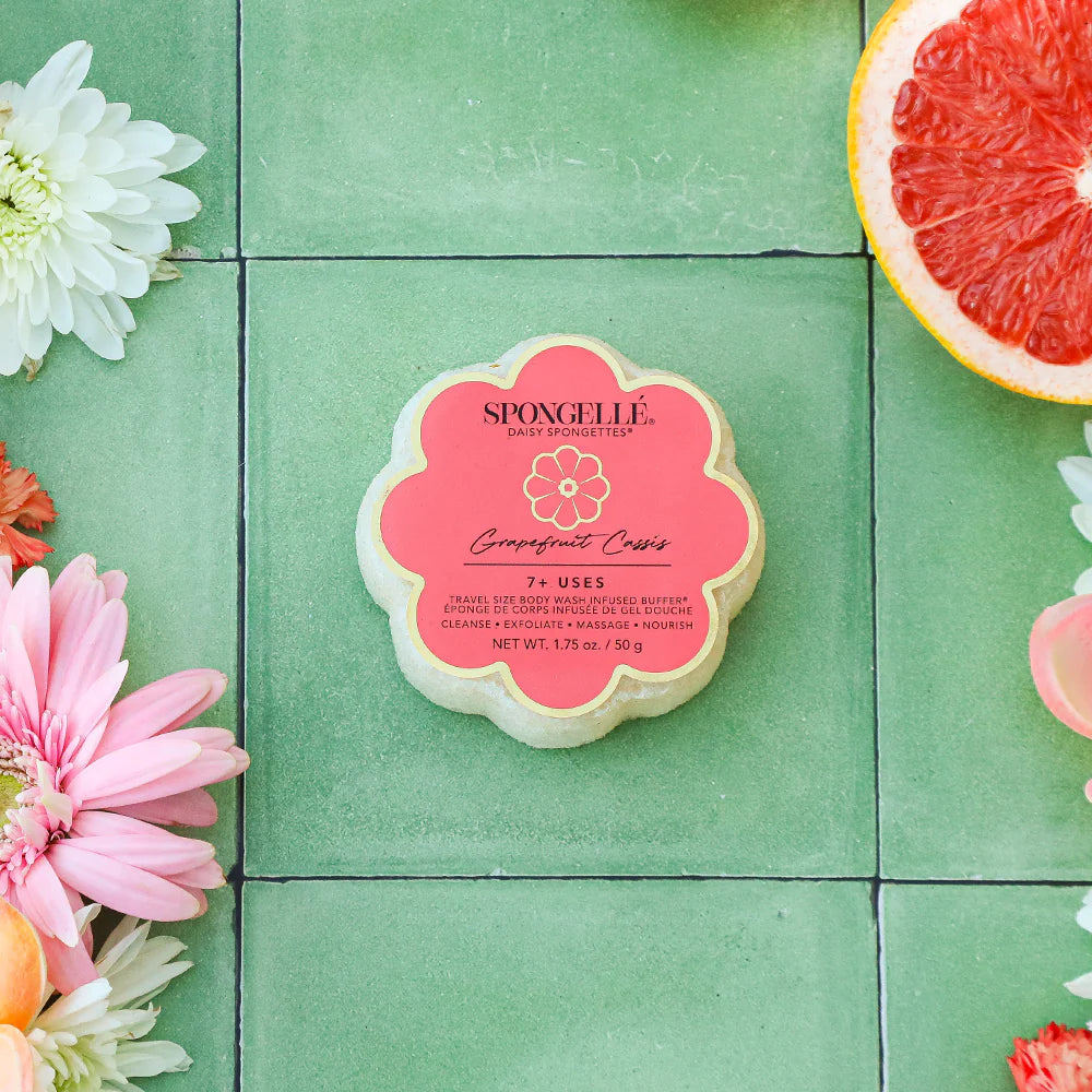Spongelle product on a green tiled background with flowers and a grapefruit slice.