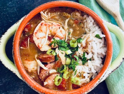 Bowl of seafood gumbo with shrimp, sausage, and rice on a blue background