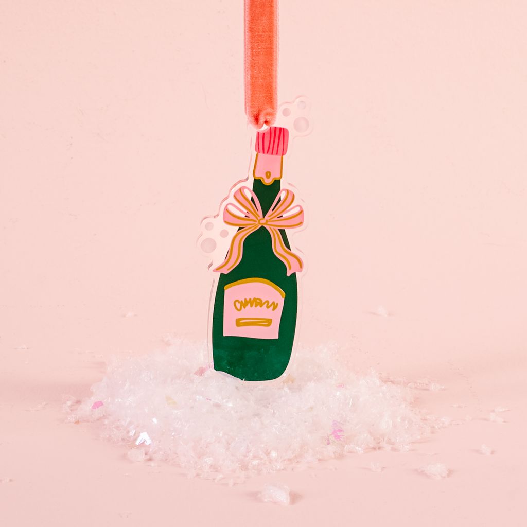 flat acrylic ornament in the shape of a green champagne bottle shown on a pink background