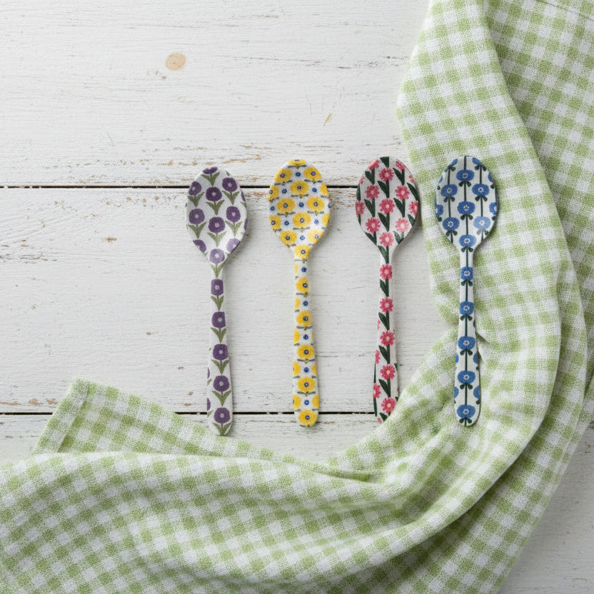 4 assorted small spoons with floral designs arranged on a wooden surface with a green gingham cloth