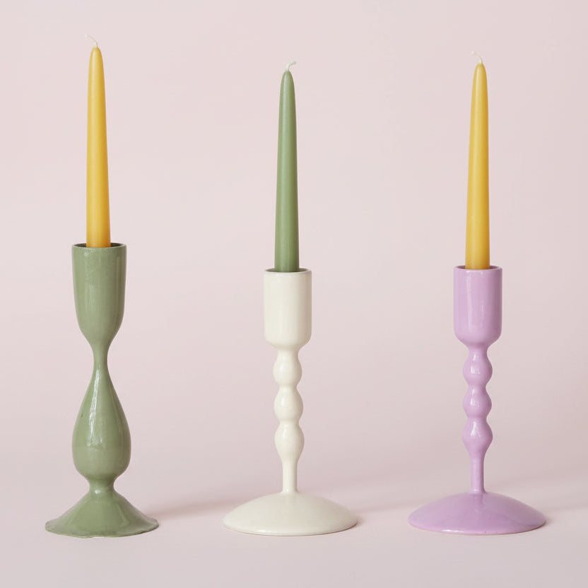 3 enameled taper candle holders in a row on a pale pink background