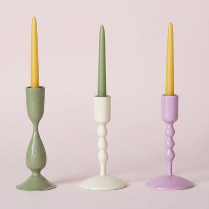 3 enameled taper candle holders in a row on a pale pink background