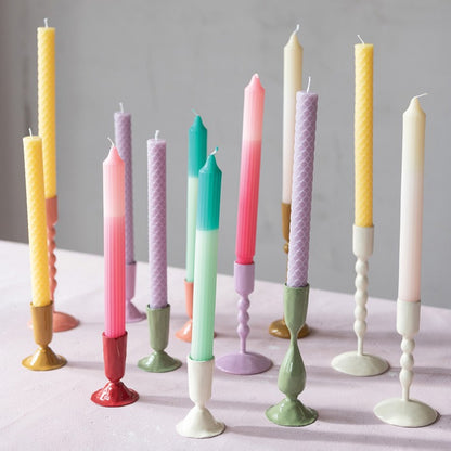 several taper holders holding multi colored candles set on a light grey surface