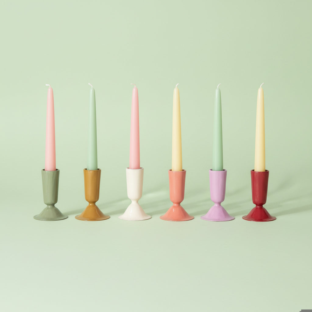 6 enameled taper candle holders in assorted colors in a row on a light green background