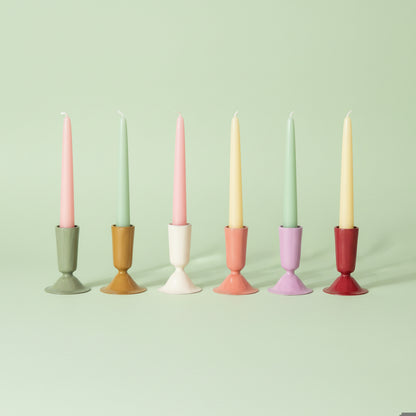 6 enameled taper candle holders in assorted colors in a row on a light green background