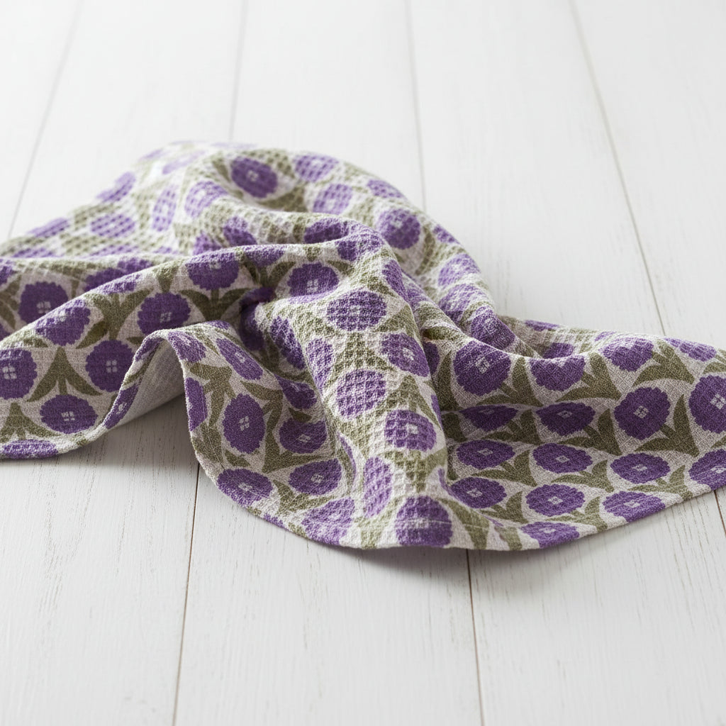 white tea towel with purple flowers and olive green leaves draped on a white wooden table