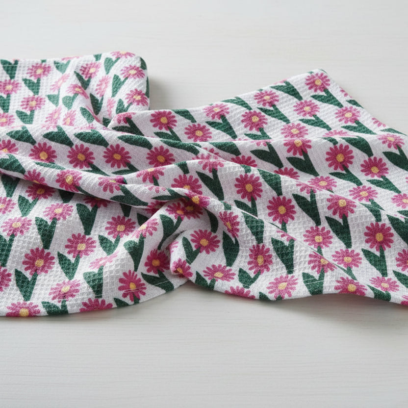 white tea towel with pink flowers and green leaves draped on a white surface