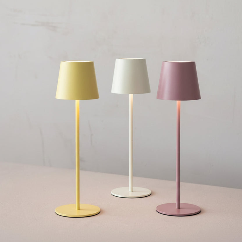 Three desk  lamps in yellow, white, and pink with colored shades on a neutral background.