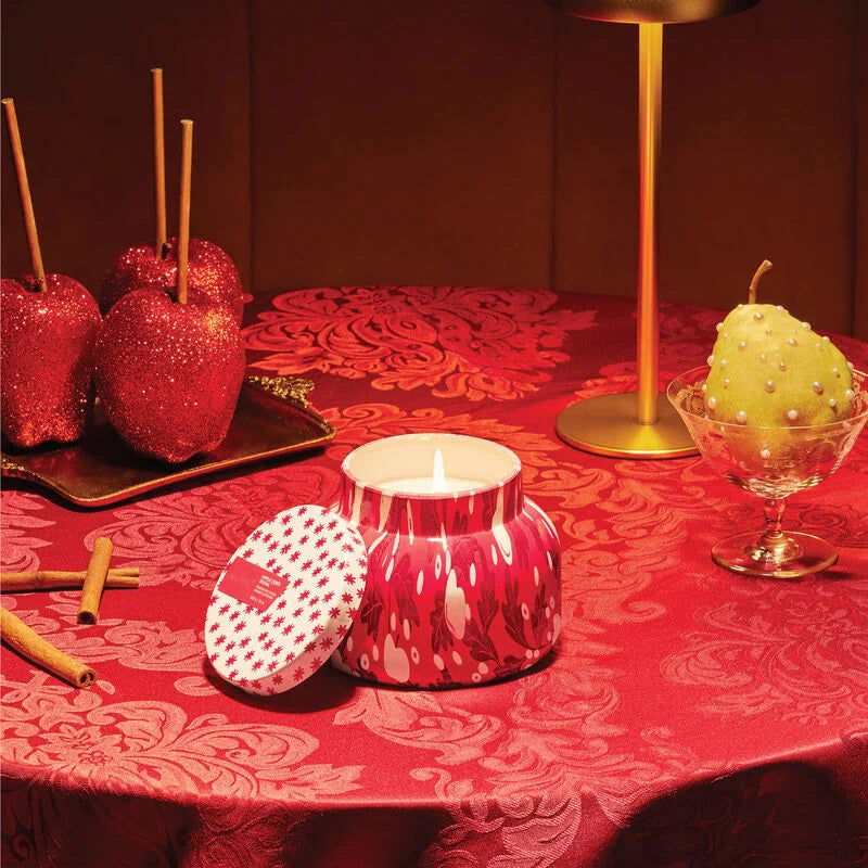 Lit apple cider social candle set on a table with caramel apples, cinnamon sticks and a pear.