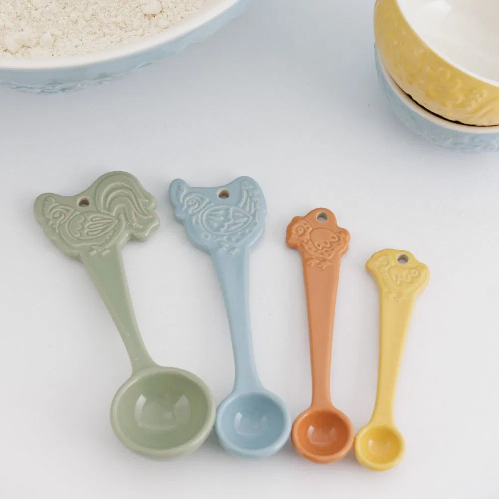 Set of four ceramic measuring spoons in green, blue, orange, and yellow on a white surface.