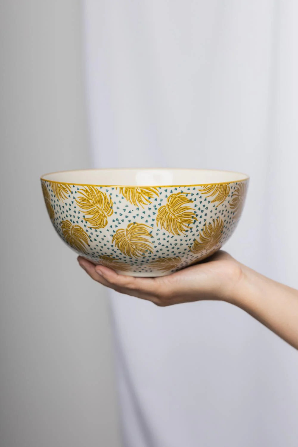 Ceramic bowl with yellow leaf pattern held by a hand against a plain background