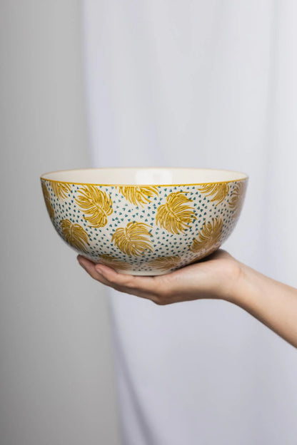 Ceramic bowl with yellow leaf pattern held by a hand against a plain background
