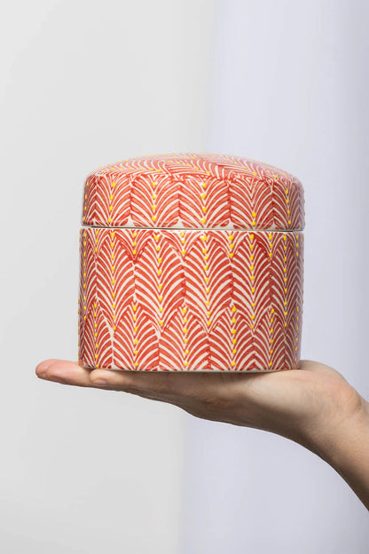 Hand holding a small cylindrical container with a vibrant, patterned design on a plain background