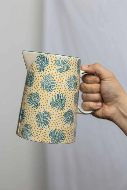 Hand holding a ceramic pitcher with leaf pattern against a plain background