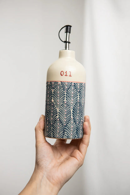 Hand holding a decorative oil bottle with a patterned design against a plain background