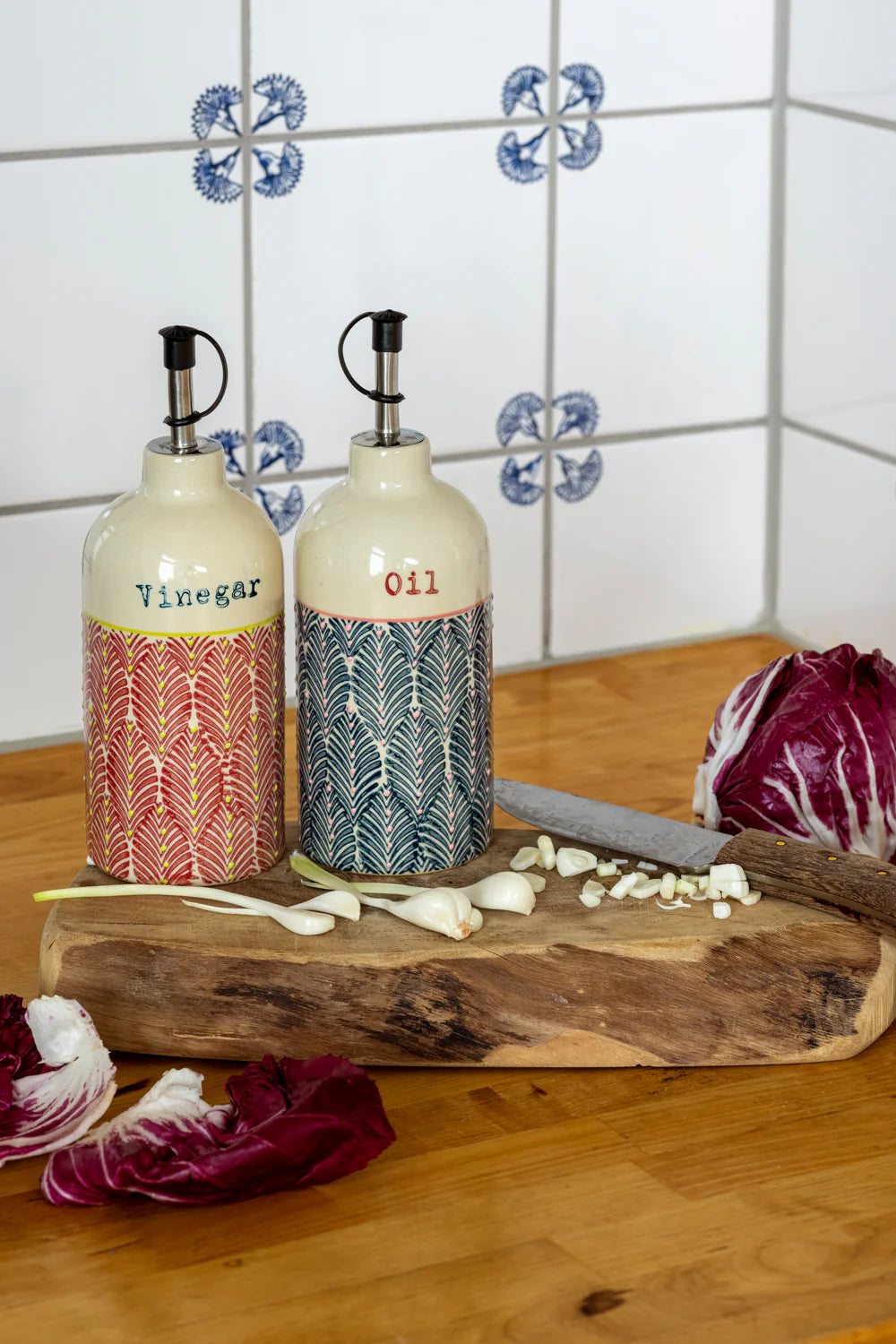 Two patterned bottles labeled 'Vinegar' and 'Oil' on a wooden cutting board with vegetables in a kitchen setting.
