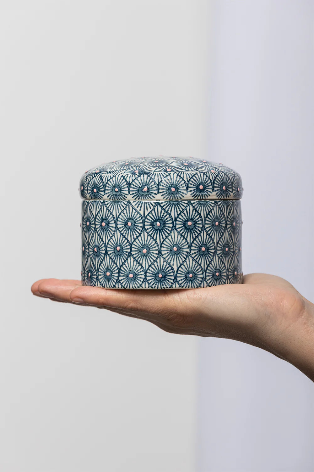 Hand holding a small decorative container with a blue geometric pattern against a plain background