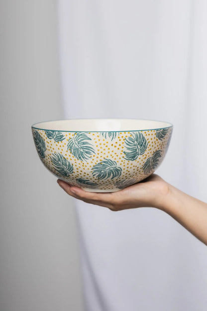 Hand holding a ceramic bowl with leaf pattern against a plain background