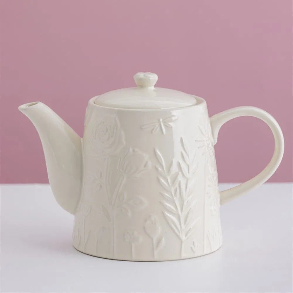 White ceramic teapot with embossed floral design on a pink background